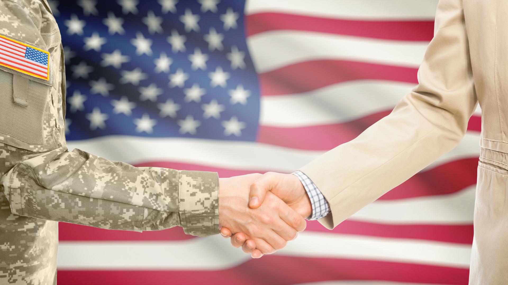 Photo of handshake between person in military uniform and person in a suit in front of an American flag